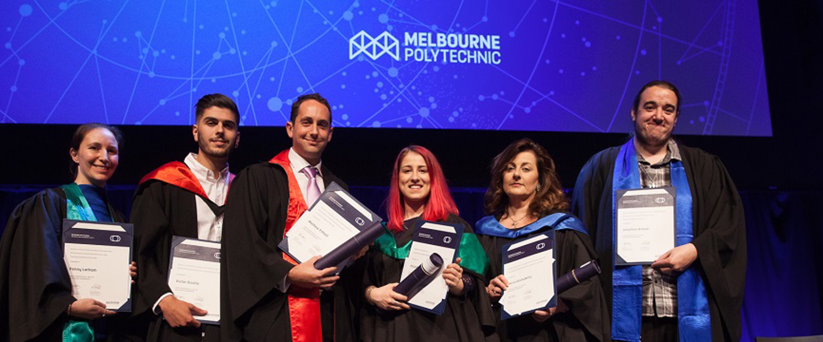 People wearing coloured robes holding graduation certificates