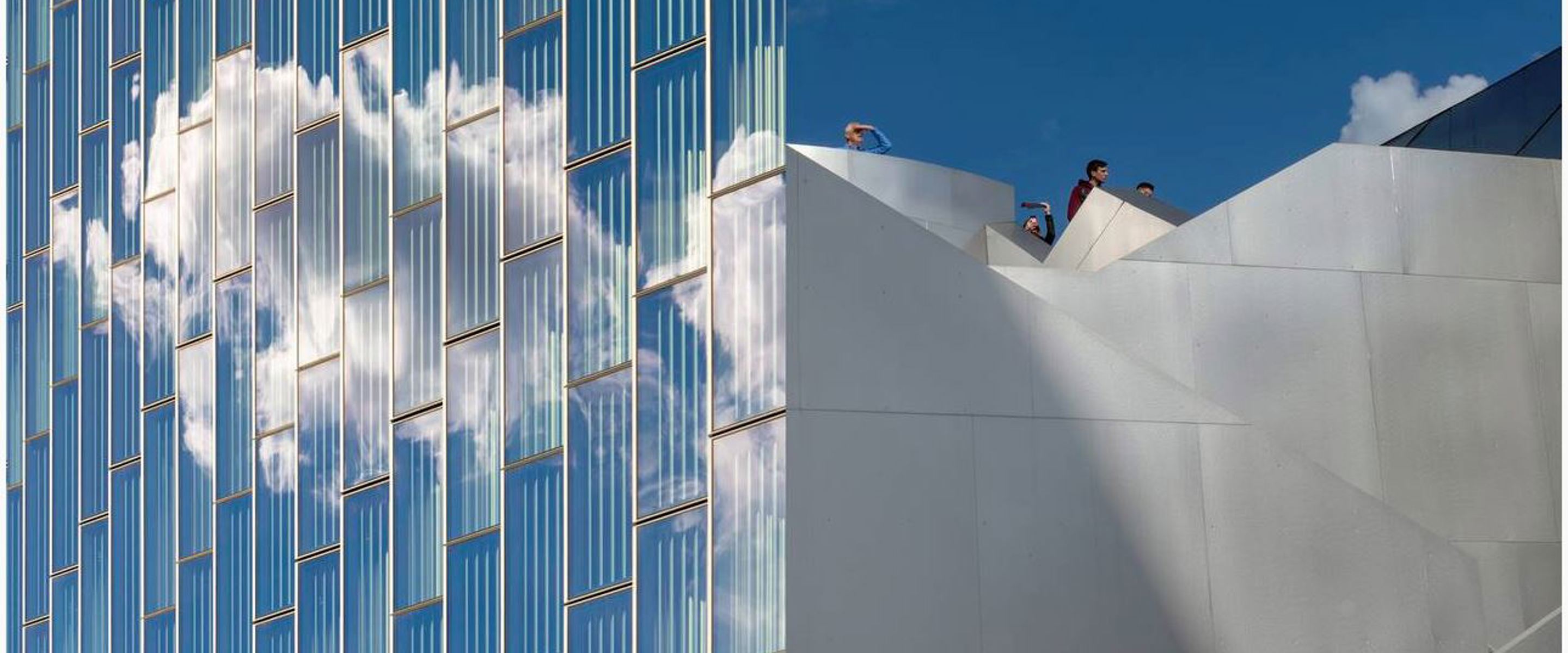 Photography artwork of building with reflective windows and people looking into distance from top of building  