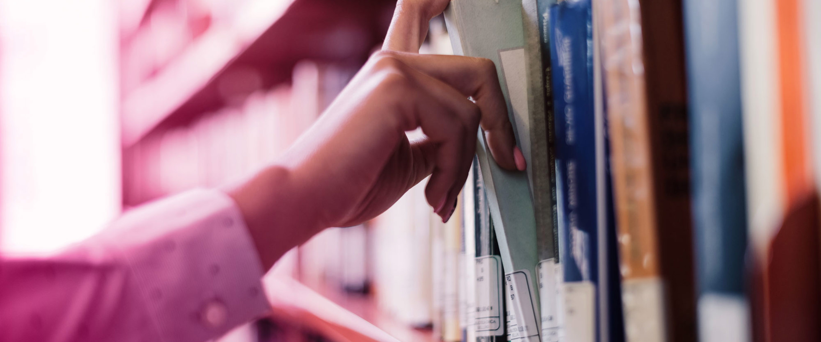 Someone grabbing a book from a library shelf