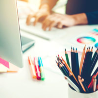 A person at a desk using a computer with coloured pencils and plans next to them