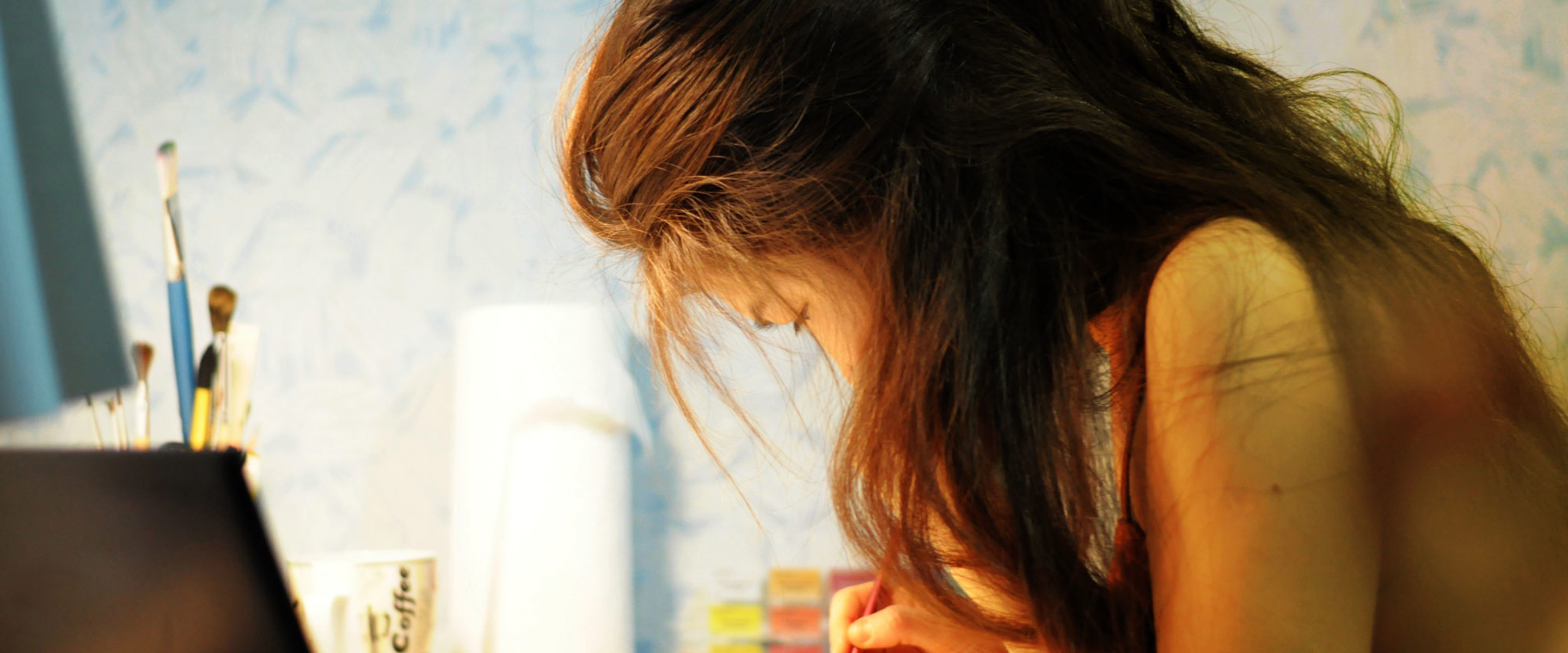 A woman sitting at a table carefully painting a picture she drew