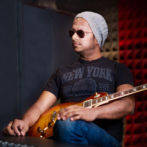 Portrait of musician at a mixing desk and an electric guitar resting on their lap