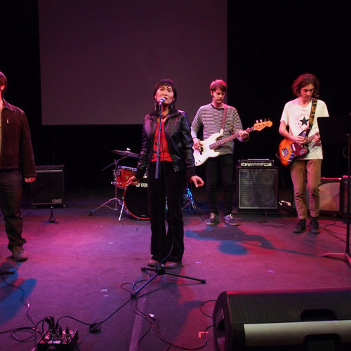 Music students singing on stage, with musicians playing saxophone and electric guitars