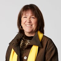 A woman wearing a brown jacket and a yellow scarf, standing confidently against a neutral background