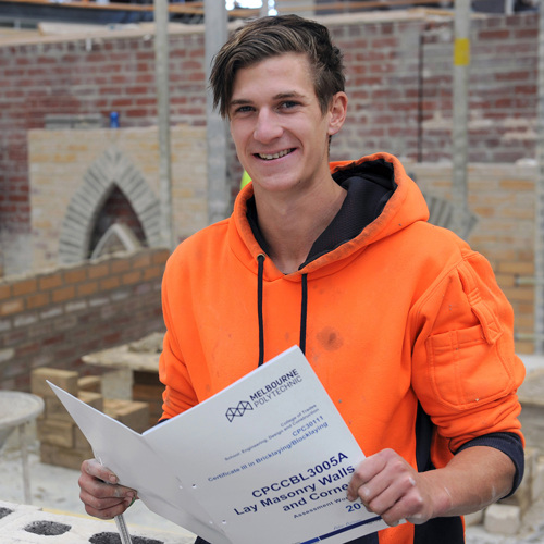 Trade student smiling at camera while holding a Bricklaying and Blocklaying manual.