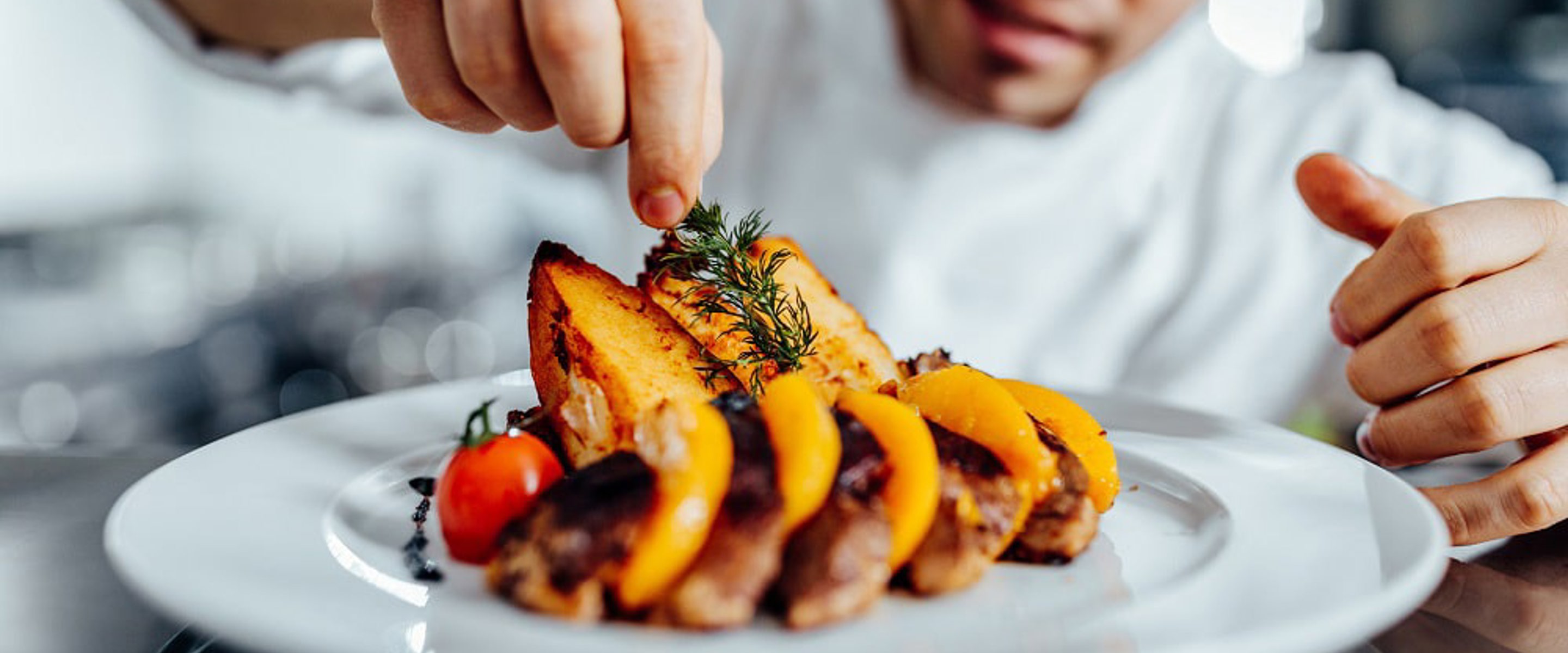 Cookery studies student garnishing roast vegetable dish with rosemary