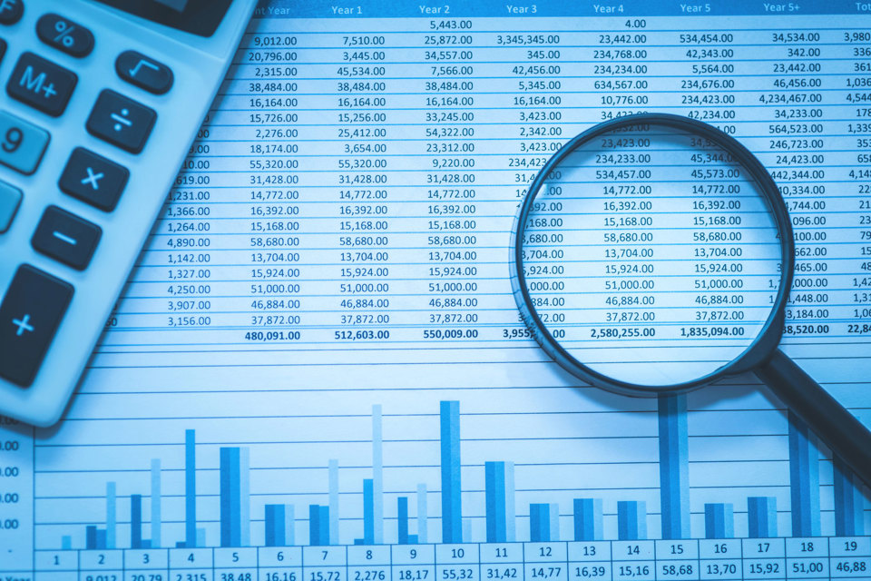 Image of statistics table and graph on a sheet of paper, with a calculator and magnifying glass.