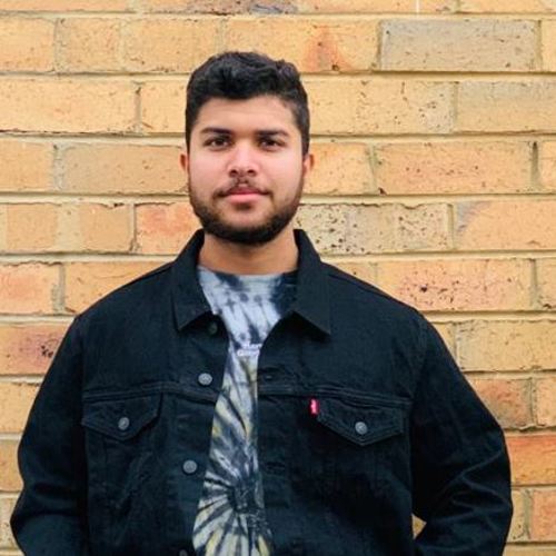 Portrait of Themiya in tie-dye t-shirt and black shirt standing in front of a brick wall