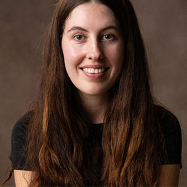 A woman with long brown hair wearing a black shirt smiling at the camera