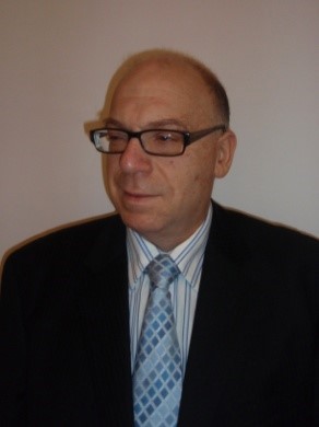 Portrait of Samuel Kaspi in a black suit with a white and light blue shirt and a matching white and light blue tie.