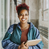 Portrait of happy female student wearing jacket holding books in college corridor