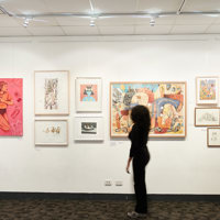 A gallery wall with student illustration artwork displayed. There are two visitors observing the art work.