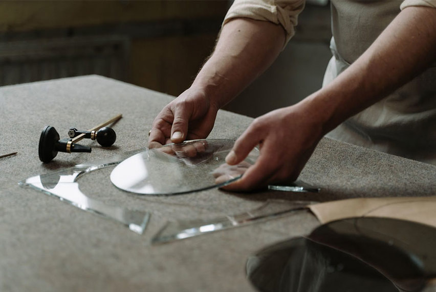 Artist's hand measuring and cutting a glass circle with tools around them