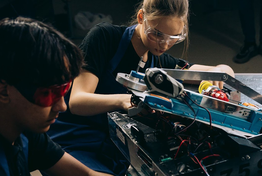 Students wearing safety gear work on a robotics project