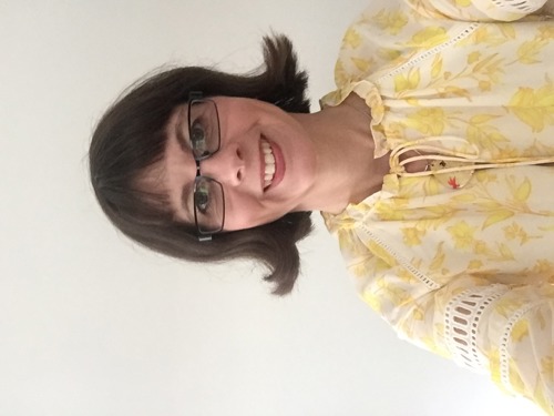 Portrait of Dr. Nicola Cooley. Smiling woman with brown hair, glasses, and a yellow floral blouse.