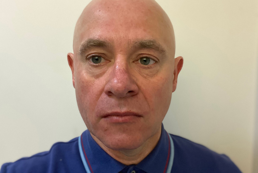 Portrait of Peter Hogg wearing a blue polo shirt with a light blue and red striped collar.