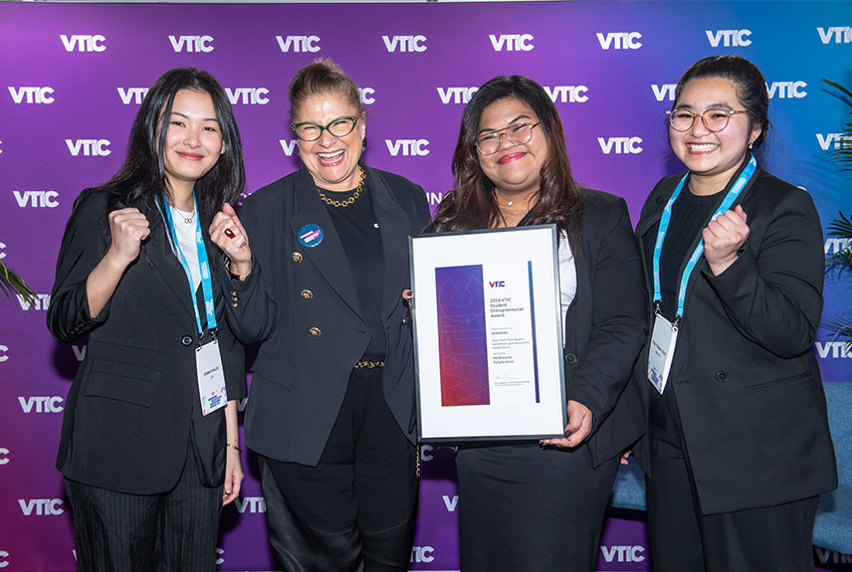 Group of four women in formal suits pose with a certificate in hand.