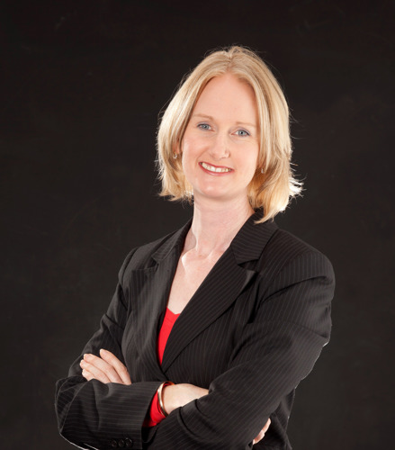 Portrait of Rachael Cowley smiling with crossed arms and wearing a suit jacket.