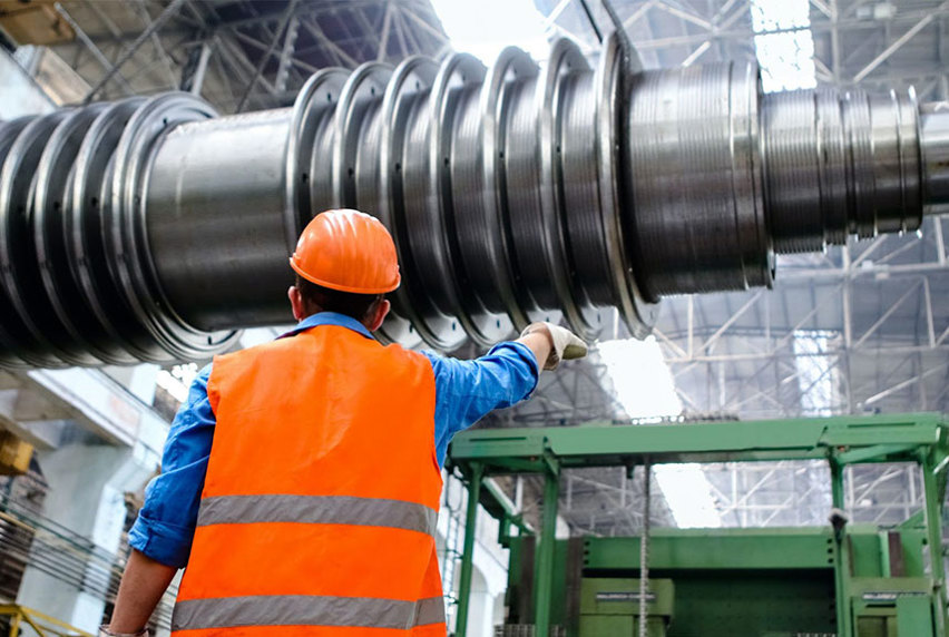 A man in an orange vest stands beside a large metal machine.