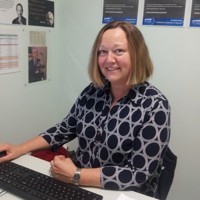 Portrait of Lou Nunn working at a desk, wearing a shirt covered in a sophisticated looking pattern of circles.