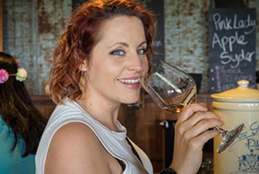 A woman with red hair smiling while holding a glass of wine at a social event.