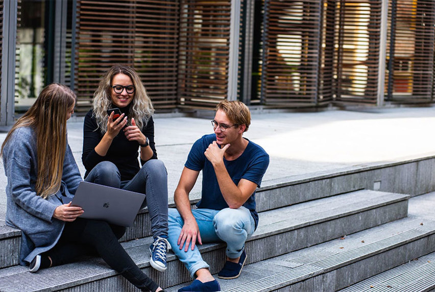 Three students gathered outside by campus steps smiling and talking